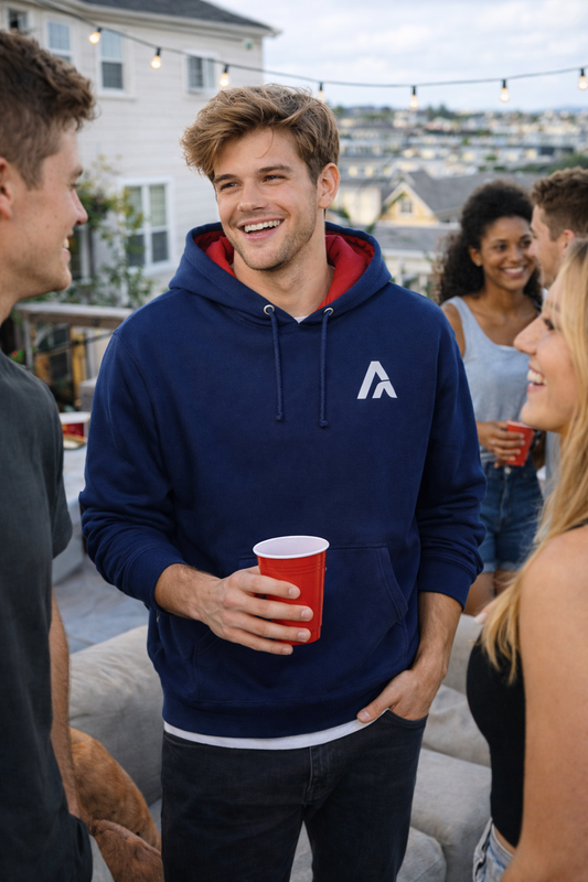 Model wearing a navy Atlas hoodie with red hood lining and white Atlas A embroidered logo, socialising with friends at an outdoor terrace gathering