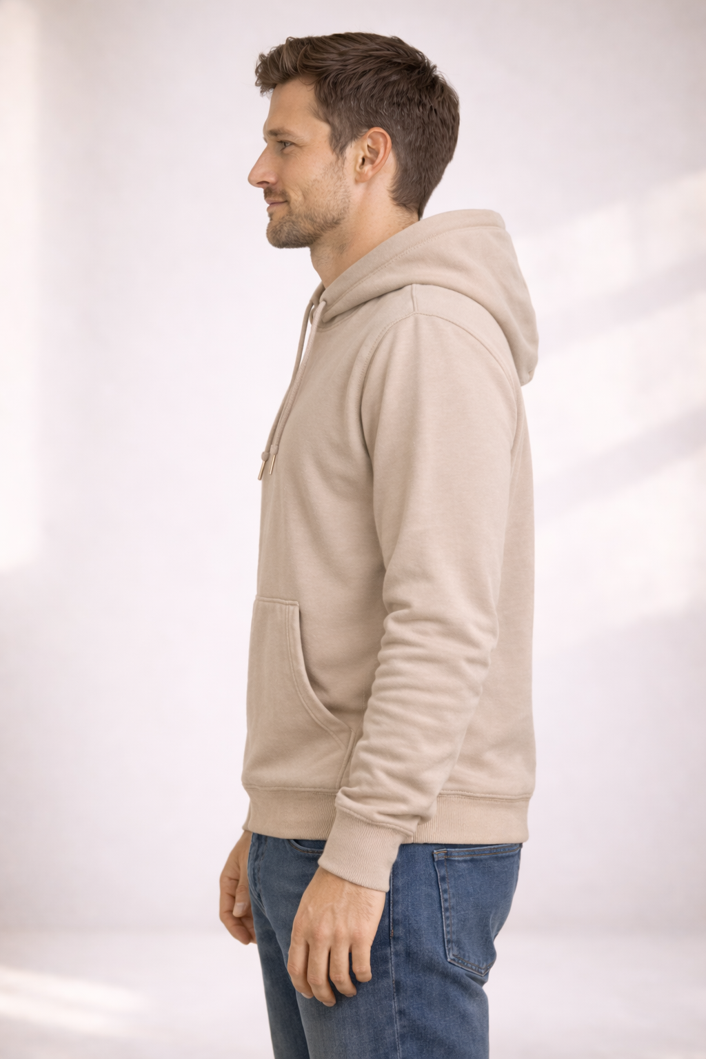 Side profile of a man wearing a light beige pullover hoodie showing relaxed fit and hood.