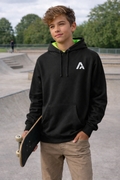Young person wearing a black hoodie with a logo, holding a skateboard at a skate park.