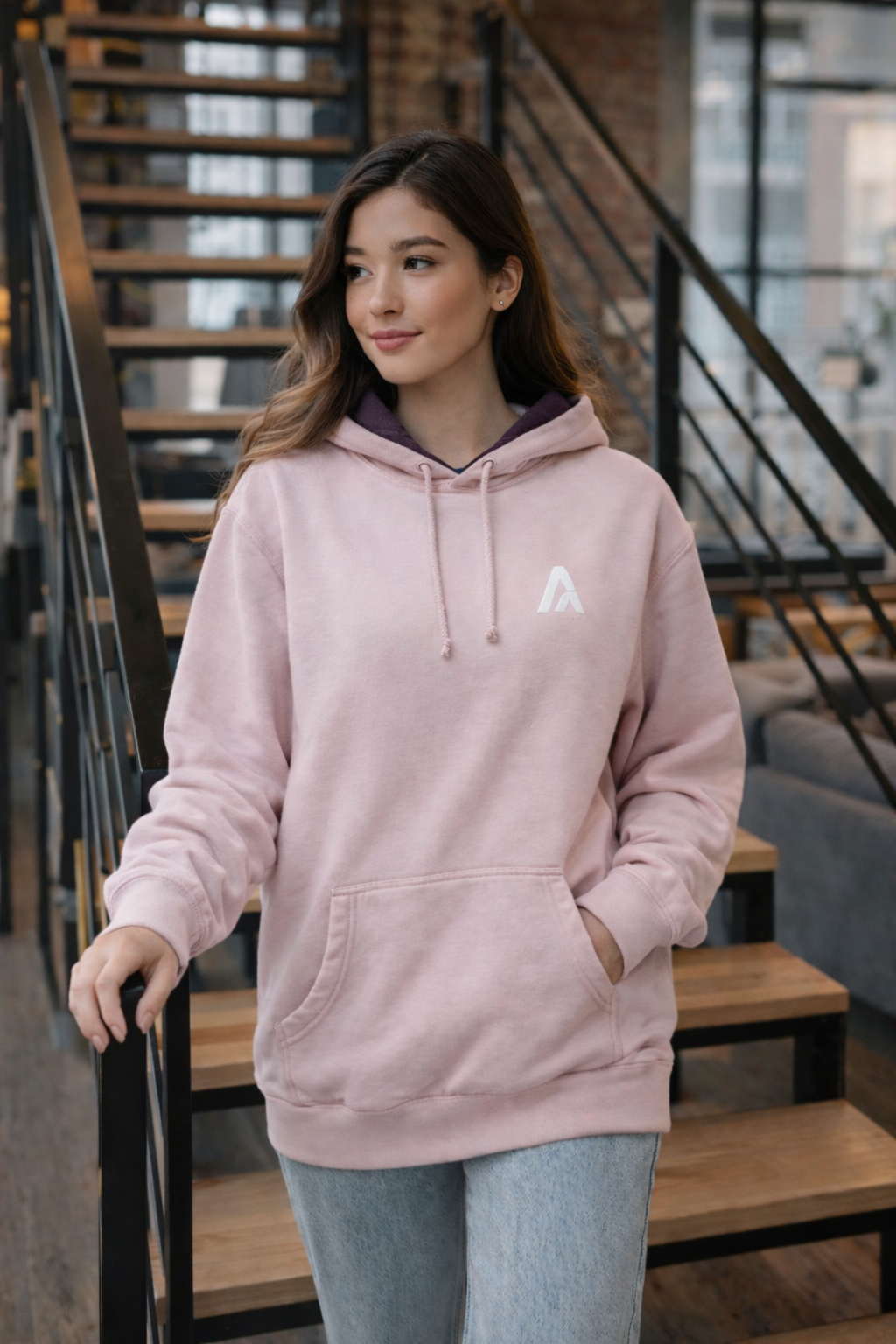Woman wearing a pink hoodie with a logo in an indoor setting