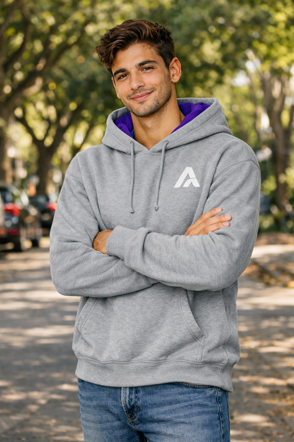 Man wearing a gray hoodie with a logo, standing outdoors with trees in the background