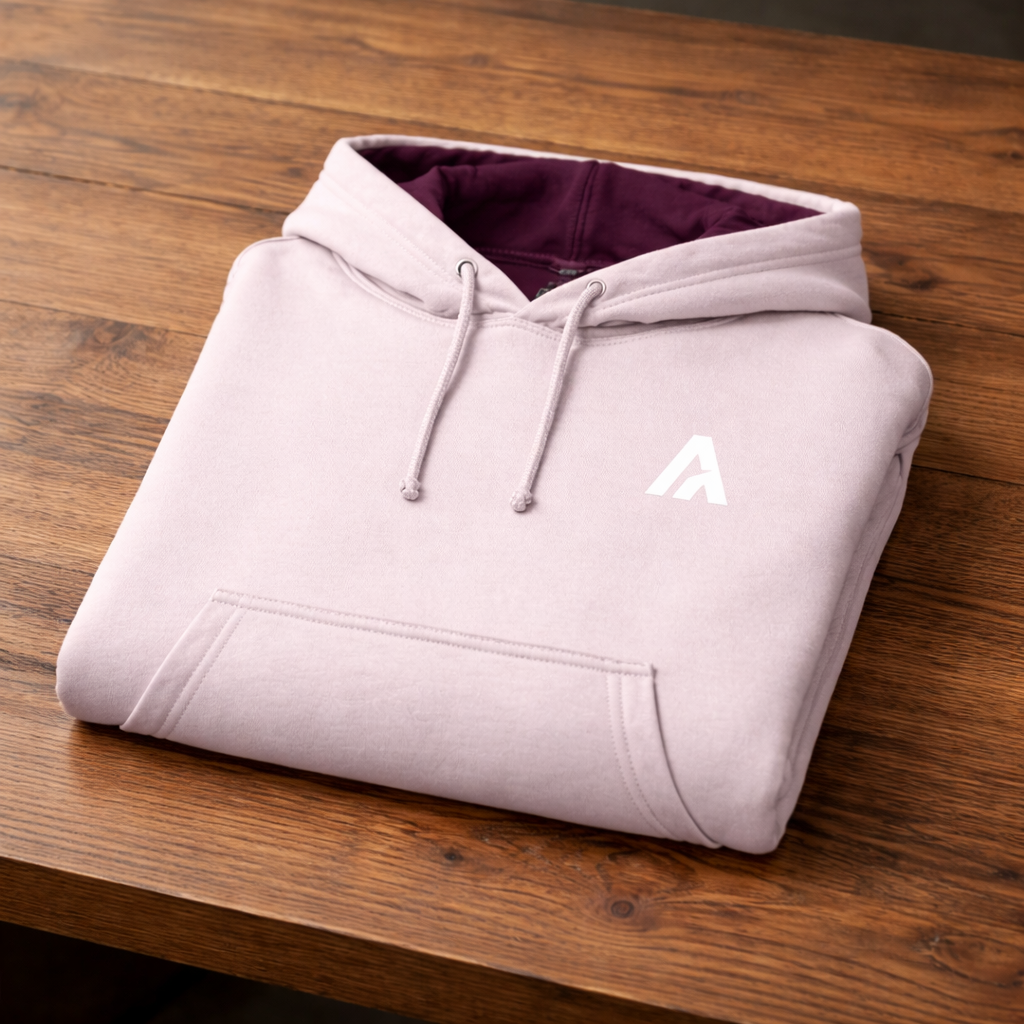 Folded light pink hoodie with a logo on a wooden surface