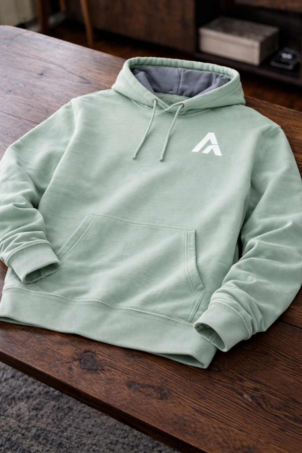 Light green hoodie with a logo on a wooden surface