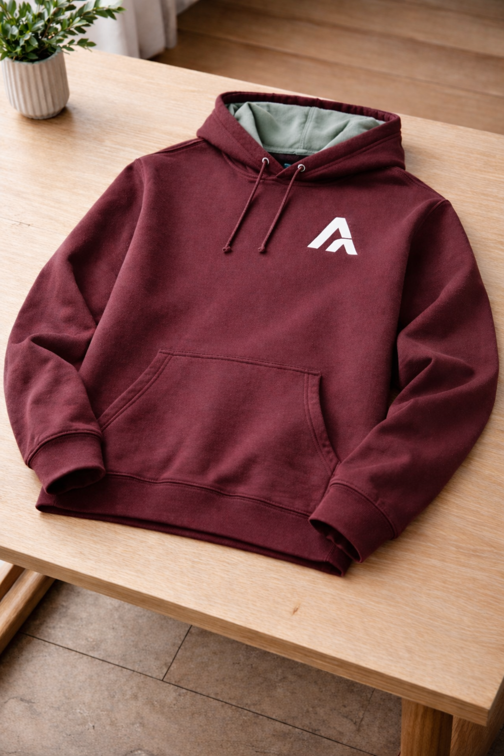 Maroon hoodie with a white logo on a wooden table