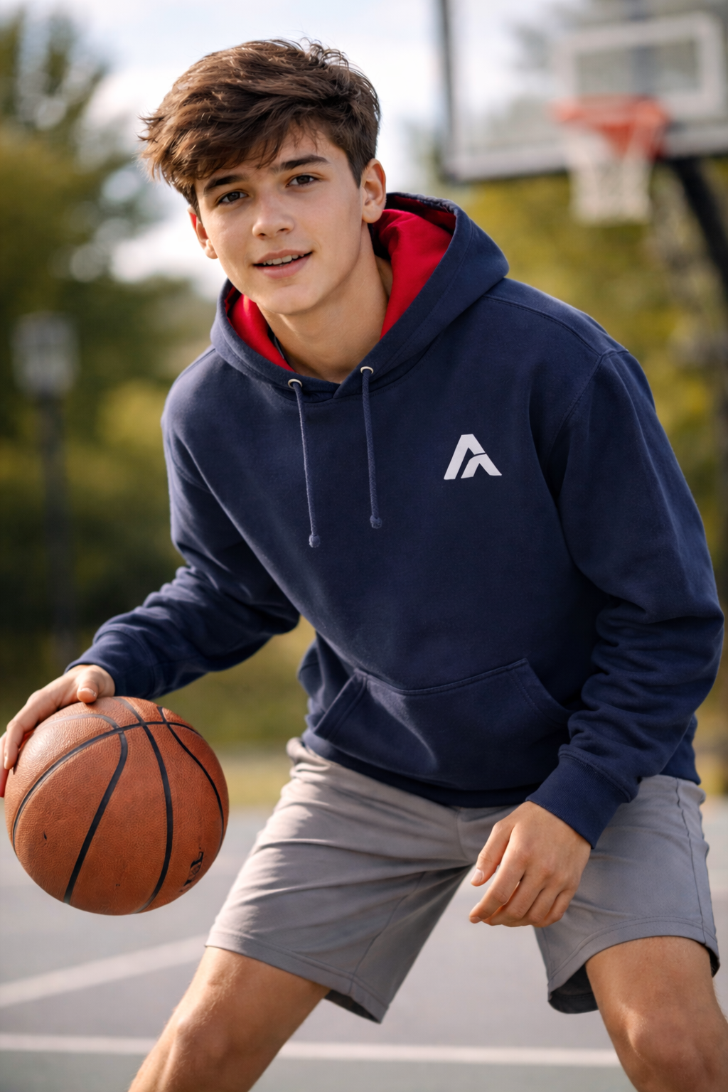 Young boy holding a basketball on a court wearing a navy hoodie with a logo.
