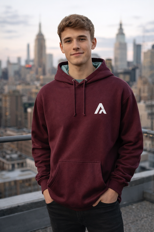Male wearing a maroon hoodie with sage hood lining and embroidered Atlas A monogram on a rooftop with city skyline