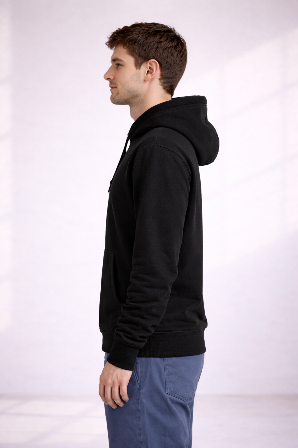 Side profile of a man wearing a black pullover hoodie showing relaxed fit and hood.