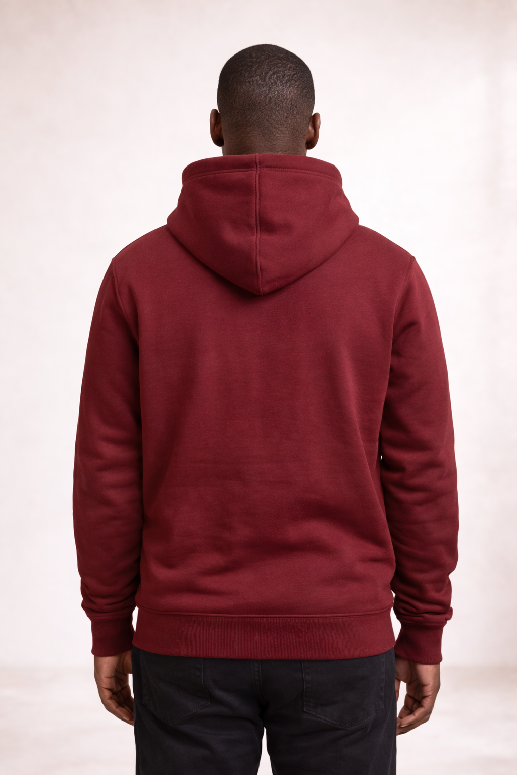 Back view of a man wearing a brick red pullover hoodie with hood and ribbed hem.