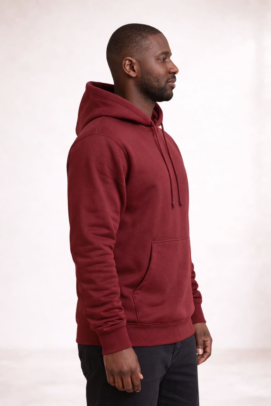 Side profile of a man wearing a brick red pullover hoodie showing relaxed fit and hood.