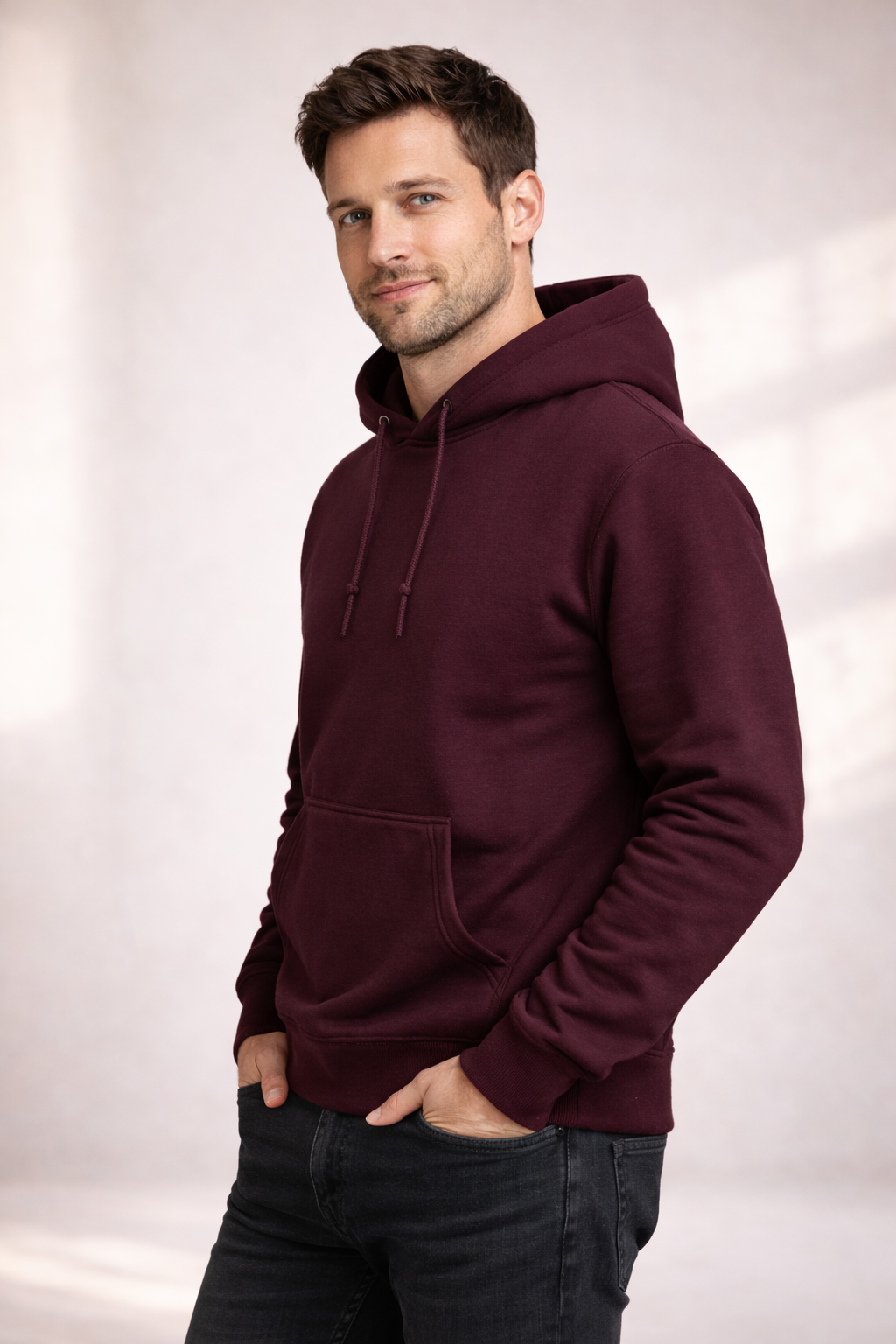 Man wearing a burgundy pullover hoodie shown in angled front view with drawstring hood and kangaroo pocket.