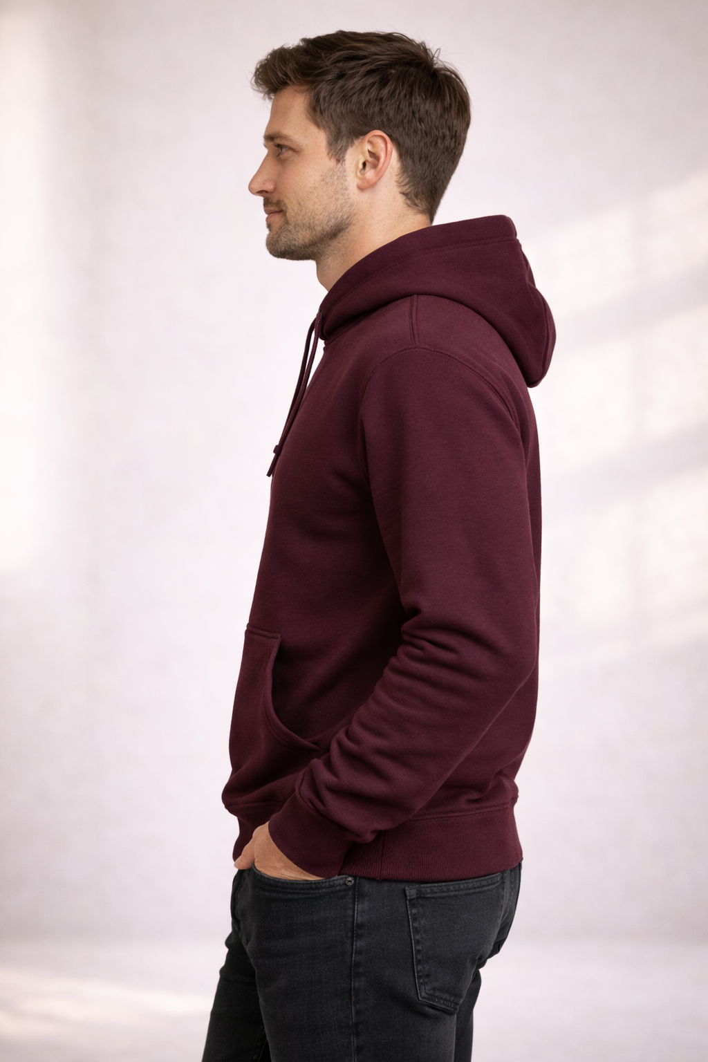 Side profile of a man wearing a burgundy pullover hoodie showing relaxed fit and hood.