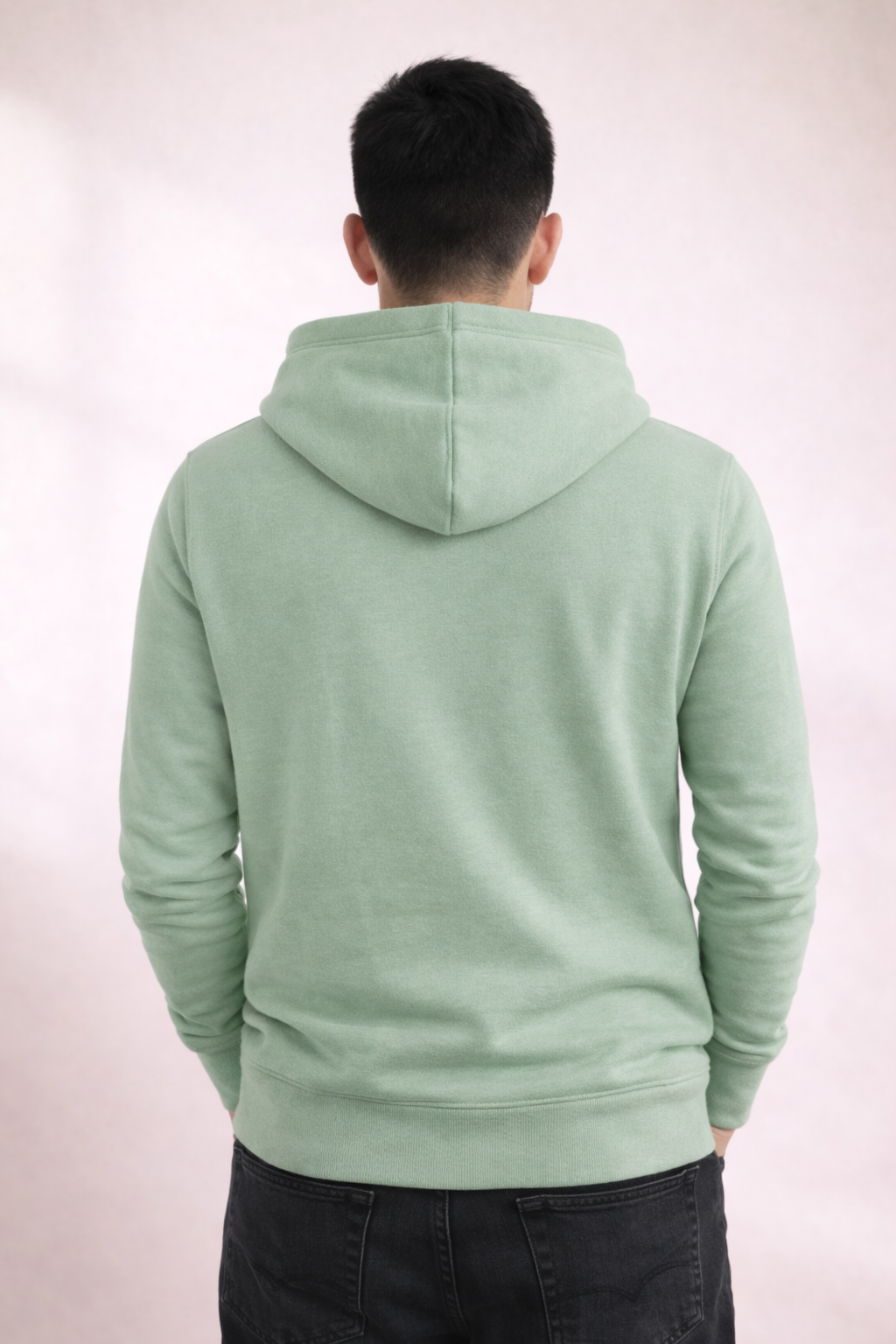 Back view of a man wearing a sage green pullover hoodie with hood and ribbed hem.