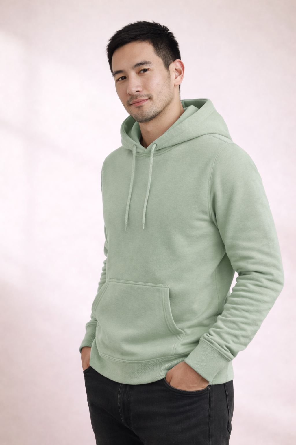 Man wearing a sage green pullover hoodie shown in front angled view with drawstring hood and kangaroo pocket.