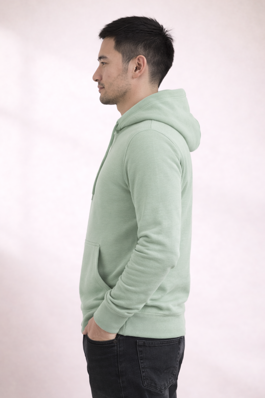 Side profile of a man wearing a sage green pullover hoodie showing relaxed fit and hood.